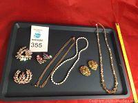 Photo of all jewelry pieces arranged on black tray with red background, showing brooches, earrings, and three necklaces.