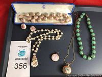 Lot contents shown on tray including porcelain bead necklace in blue box, faux pearl necklace, glass teardrop pendant, small floral pendant, enamel locket necklace, green glass bead necklace and earrings