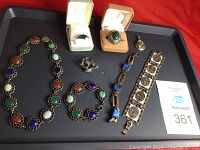 Full jewelry lot arranged on a black tray on a red surface, including necklace, bracelets, rings, earrings, and brooch.
