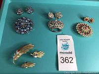 Top view showing all four sets of brooches and matching earrings laid out on a flat surface with auction tag.