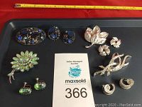 Photo showing all vintage brooches and earrings arranged on a black tray with a ruler above for size reference.
