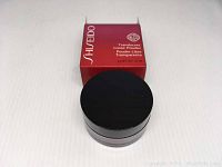 Round black container of Shiseido translucent loose powder in front of box, product container with lid on.