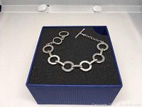 Swarovski silver-tone bracelet with circle and rectangular links displayed on a black foam insert within a blue box, showing the overall design and toggle clasp.
