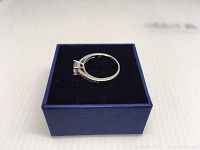 Side view of Swarovski ring in blue jewelry box on white surface showing the band and crystal setting.