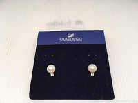 Close-up of Swarovski earrings with visible crystal pearl and small clear stone on Swarovski card.