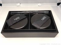 Two round NARS compacts with elastic straps and a makeup brush in a black tray resembling a bento box.