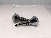 Two silver-tone faceted wine stoppers with polygonal tops and rubber rings to seal bottles, lying on a white surface.
