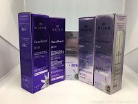 Five boxed NUXE Paris Nuxellence anti-aging skincare products arranged in a row showing front and partially sides of the boxes. Includes Detox, Éclat, and Eye Area products.