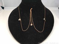 Layered rose gold-tone necklace displayed on black stand showing pear-shaped Swarovski crystals and chain extender with crystal charm.
