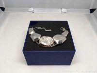 Silver Swarovski atelier wristband placed on black foam inside a blue box, showing three large faceted clear crystals linked in a chain with lobster clasp and extension chain.