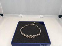 Silver tone Swarovski bracelet with heart-shaped clear crystals displayed on black foam in blue box.