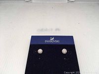 Pair of Swarovski round crystal stud earrings in gold-tone setting on a Swarovski branded black and blue card holder.