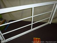 White metal adjustable security bar laid flat on a surface showing the front view with horizontal and vertical support bars.