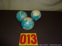 Three used five pin bowling balls with blue and white swirled coloration on a dark surface.