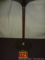 Full view of the base of the stand showing the round flat stable bottom and slender wooden shaft.