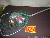 Photo of large fishing net with metal handle and multiple fishing bobbers packed in plastic bags inside the net.
