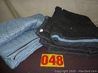 Photo of two folded moving blankets, one blue and one black, stacked showing thickness and texture