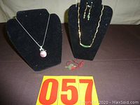 Overall photo showing two necklaces displayed on black velvet stands, pair of earrings attached to one necklace, small dragon figurine in front, and lot number card.