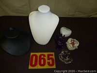 Photo of two necklace display busts (white and black), a purple hand-shaped ring holder, two decorative trinket boxes (heart and oval shapes), and a metal ring sizer set all arranged together on a tablecloth.