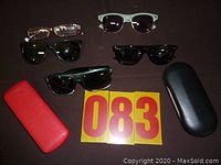 Wide view of all glasses and cases on a flat surface including four pairs of sunglasses, one pair of reading glasses and two cases