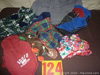 Photo of five small dog coats, gray dog bed, brown plush toy, and red knit hat on dark surface.