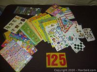 Full view of a wide assortment of different sticker sheets laid out on a dark surface, showing various characters, colors, and sizes of the stickers.