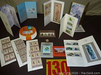 Wide view image showing multiple philatelic items including sheets, folders, booklets, and loose stamps arranged on a surface.