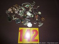 Overview photo of assorted jewelry items laid out on dark surface including necklaces, pendants, bracelets, rings, and small parts.