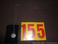 Sterling silver locket on fine chain displayed on black background with auction number cards