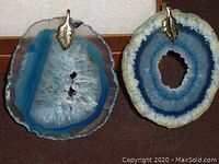 Close-up photo of two blue agate crystal pendants showing crystalline centers with leaf-shaped metal bails.