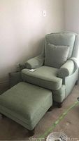 Photo of green upholstered sitting chair with one cushion and matching foot stool showing overall condition and style.