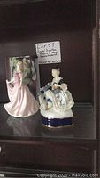Two collectible figurines on shelf with a handwritten label showing lot details.