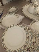 Top view of seven larger plates with floral and gold trim border, one chipped plate visible.