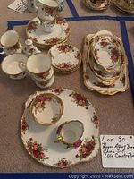 Photo of the tea cups, saucers, small plates, sugar bowl, and creamer pitcher arranged on carpet.