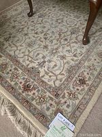 Photo showing the fringed edge of the ivory background oriental rug with floral pattern and wooden table leg on top.