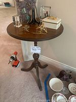 Full view of the round antique wooden pedestal table showing tabletop and base, with decorative items on top (not included).