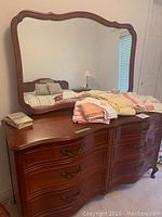 Women's dresser with attached mirror and assorted linens on top, cherry finish and brass hardware visible