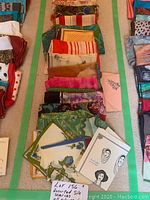 Photo shows a collection of silk scarves arranged in rows on a light carpet. Visible various colors and patterns including floral, stripes, and abstract designs.