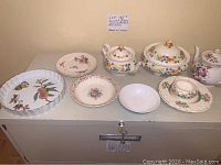 Full view of assorted bone china dinnerware pieces on table showing plates, bowls, covered tureens, and cup and saucer