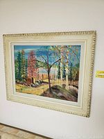 Front view of framed landscape painting showing colorful trees, path, and rocks in decorative cream frame.