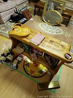 Wide view of the large wooden cribbage board with smaller heart-shaped cribbage boards on top and various items underneath including decks of cards and teddy bears.