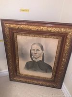 Framed vintage portrait of a woman leaning against a wall, ornate frame with gold accents, photo also shows size label indicating dimensions (H:31, W:26, D:1.5 inches).