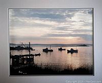 Framed color photograph featuring silhouetted boats on calm water at sunset with artist signature.