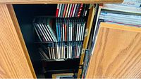 Front view of wooden shelving unit door partially open showing several rows of CDs in jewel cases inside