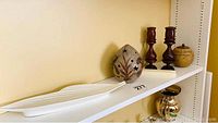 White leaf-shaped serving dish on a shelf with a small decorative ceramic pot and two wooden candle holders with candles beside it.