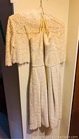 Full view of the vintage 1962 wedding dress hanging on a hanger showing long lace sleeves and the lace patterned fabric.