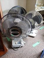 Three oscillating table fans together on carpet showing size and grill types.