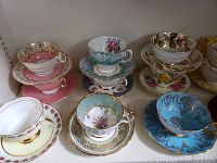 Front view of six mismatched tea cup and saucer sets on shelf