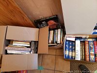 Top view of three boxes filled with various books, including Greek myths, philosophy, British history, and woodworking titles.