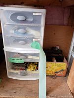 Plastic 5-drawer storage cart with labels on drawers and nearby cardboard box with items